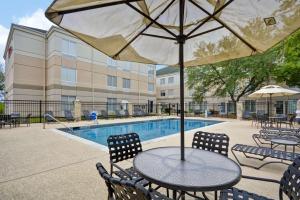 Hilton Garden Inn Austin Round Rock في راوند روك: طاولة مع كراسي ومظلة بجانب مسبح