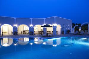 a pool at night with tables and chairs around it at Maistros Village in Karterados