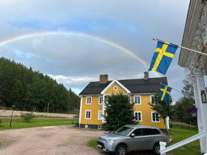 a rainbow over a yellow house with a car and flags at Värdshuset Lugnet in Malung