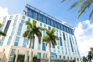 a tall white building with palm trees in front of it at Hilton West Palm Beach in West Palm Beach