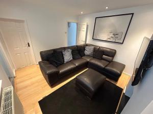 a living room with a brown leather couch and stool at Modern & Bright 4 Bedroom Home in Stoke on Trent