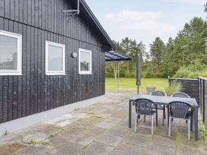 um pátio com uma mesa e cadeiras ao lado de um edifício preto em 6 person holiday home in S by em Sæby