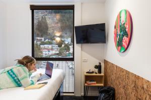 a woman laying on a bed using a laptop at LyLo Queenstown in Queenstown