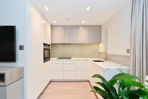 cocina con armarios blancos, TV y planta en Luxury 3 Bed Mayfair Apartment, en Londres