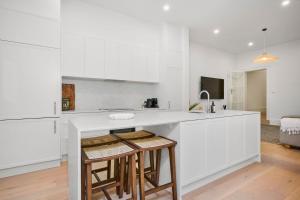 una cocina con armarios blancos y un bar con taburetes en Cozy North Melbourne Family Retreat, en Melbourne