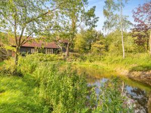a house in the woods with a river in the foreground at Linen Post Barn in Debenham