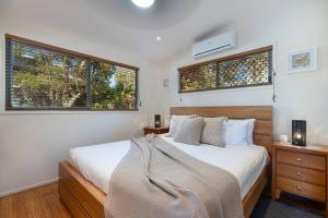 a bedroom with a bed and two windows at Delightful Dicky Beach Holiday House in Caloundra