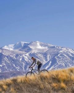 Hotel De Cielo في توبونغاتو: رجل يركب دراجة على تلة مع جبل مغطى بالثلج
