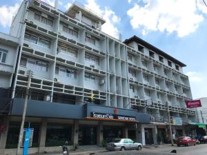 Srivichai Hotel في ناخون راتشاسيما: مبنى ابيض كبير فيه سيارات تقف امامه