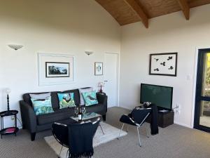 a living room with a couch and a tv at Kākā Ridge Retreat Luxury Cottage in Tawharanui