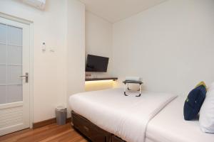 una camera da letto bianca con un letto e una televisione di Urbanview Hotel Groovy Inn Tangerang a Buaran Altre 14 foto