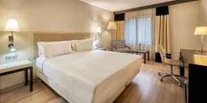 um quarto de hotel com uma grande cama branca e uma secretária em NH Lleida Pirineos em Lleida
