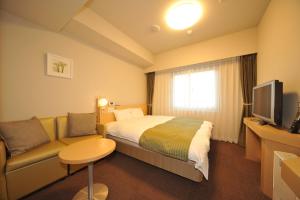 a hotel room with a bed and a couch and a television at Dormy Inn Obihiro in Obihiro