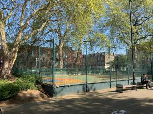 une femme assise sur un banc à côté d'un court de tennis dans l'établissement The Melville Hotel by Rokxy- Kings Cross, à Londres