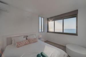 a white bedroom with a large bed and a window at Beachfront apartment with breathtaking sea view in Netanya