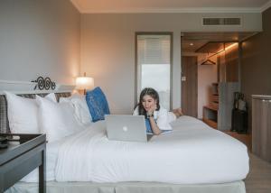 a woman sitting on a bed with a laptop at The Grand Riverside Hotel in Phitsanulok