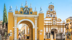 a yellow building with an arch and a church at Macarena Muralla Encantada in Seville