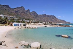 a beach with rocks and a city and mountains at Brighton Court in Campsbay on the beach. in Cape Town