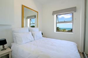 a white bed in a bedroom with a window at Brighton Court in Campsbay on the beach. in Cape Town