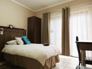 a bedroom with a bed with white sheets and blue pillows at Andante Guesthouse Klerksdorp in Klerksdorp