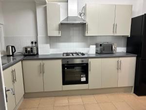 La cuisine est équipée de placards blancs et d'un four avec plaques de cuisson. dans l'établissement 3 bedroom house with garden in Tottenham london, à Londres