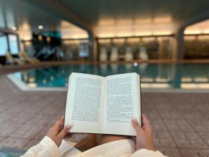 a person reading a book in front of a swimming pool at Appartementhaus Birkenwald in Seefeld in Tirol