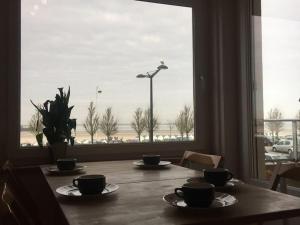 une table avec des tasses et des soucoupes dans une pièce avec une fenêtre dans l'établissement Nausicaà, Apmt bord de mer, 3ch, garage privé, à Boulogne-sur-Mer