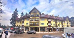 a large yellow building with cars parked in a parking lot at Arboro Royal Plaza in Borovets