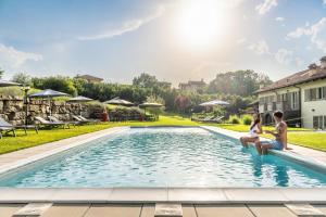 2 personnes assises au bord d'une piscine dans l'établissement Resort Limax Acis, à La Morra