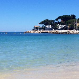 a beach with blue water and a house in the background at Lovely 4-person apartment 200 m from beaches Cap d'Antibes in Juan-les-Pins
