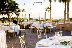 Cape Rey Carlsbad Beach, A Hilton Resort & Spa في كارلسباد: مطعم بالطاولات البيضاء والكراسي والنخيل