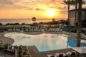 una gran piscina con sillas y el océano al atardecer en Cape Rey Carlsbad Beach, A Hilton Resort & Spa, en Carlsbad