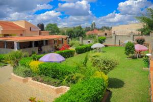 a garden with umbrellas and bushes in front of a building at Jatheo Hotel Rwentondo in Mbarara