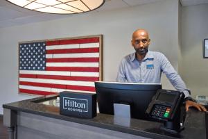 アレクサンドリアにあるHampton Inn & Suites Alexandria Old Town Area Southの電話を持つ机の前に立つ男