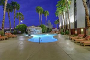 a swimming pool with chairs and palm trees at night at Hampton Inn Tropicana in Las Vegas
