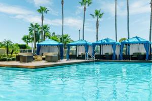 einen Pool in einem Resort mit blauen Sonnenschirmen und Palmen in der Unterkunft DoubleTree by Hilton Orlando Airport Hotel in Orlando