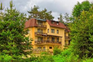a yellow building with a red roof and trees at Guest House Slunchev Cviat in Tsigov Chark