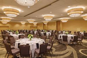 una sala de banquetes con mesas y sillas blancas y lámparas de araña en Hilton Kansas City Airport en Kansas City