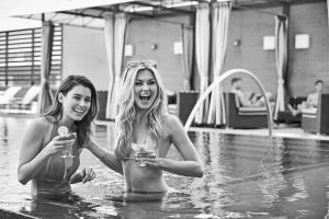 two women in a swimming pool holding wine glasses at The Highland Dallas, Curio Collection by Hilton in Dallas