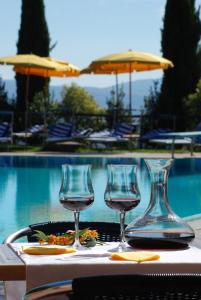 three wine glasses sitting on a table next to a pool at Casanova - Wellness Center La Grotta Etrusca in San Quirico dʼOrcia