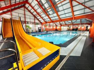 a large swimming pool with a yellow slide in a building at Three Jays in Saint Osyth