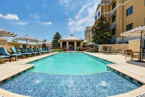 a swimming pool with chairs and umbrellas next to a building at Homewood Suites by Hilton Dallas/Allen in Allen