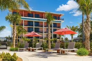 un hotel con palmeras, sillas y sombrillas rojas en Hilton Garden Inn St. Pete Beach, FL en St Pete Beach
