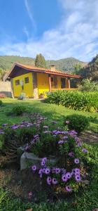uma casa amarela com flores roxas no quintal em Pousada VISTA LINDA em São Bento do Sapucaí