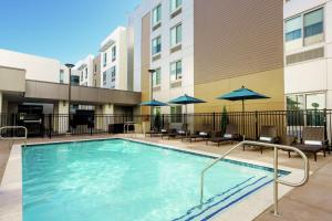 聖荷西的住宿－聖何塞北部希爾頓惠庭套房酒店，一座带椅子和遮阳伞的游泳池位于一座建筑旁边