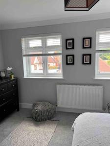 a bedroom with a bed and a dresser and two windows at Bright and Cosy Home in Southend-on-Sea