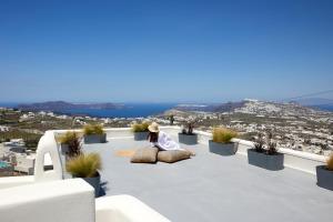 a woman sitting on a patio looking out over a city at Arxegono Cave Houses Santorini in Pirgos