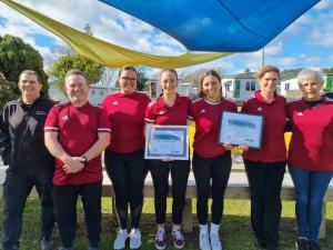 a group of people in red shirts holding certificates at Whakatane Holiday Park in Whakatane