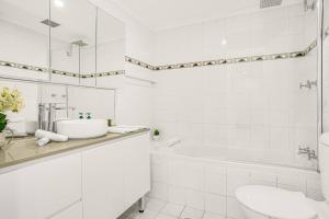 a white bathroom with a sink and a tub and a toilet at 'The Crows Nest' Spacious Studio with Balcony in Sydney