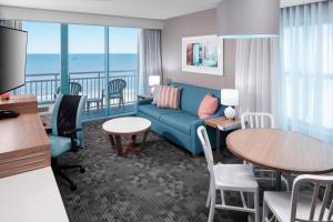 維吉尼亞海灘的住宿－弗吉尼亞海濱海灘/南萬怡酒店，带沙发和桌子的客厅以及带阳台的客房。